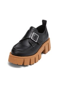 Chaussure en cuir noir avec une épaisse semelle en plateforme texturée tan, dotée d'une large sangle et d'un détail de boucle métallique sur le dessus.