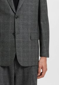 Blazer grigio a quadri realizzato in tessuto texturizzato, caratterizzato da due bottoni neri, rever a punta e una tasca sul petto.