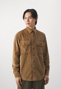 Brown corduroy shirt with a button-up front, two chest pockets, and a collar; features vertical stripes and dark buttons.