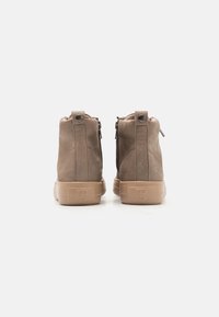 Bottines en daim marron avec une texture lisse, dotées de fermetures éclairs à l'arrière, d'un bout arrondi et d'une semelle en caoutchouc beige clair.