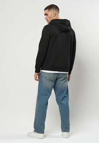 Melns kapuču džemperis, kokvilnas maisījums, brīvs piegriezums, riboto aproču apdare, valkāts ar gaiši zili izbalējušiem džinsa džinsiem un baltām sporta kurpēm.