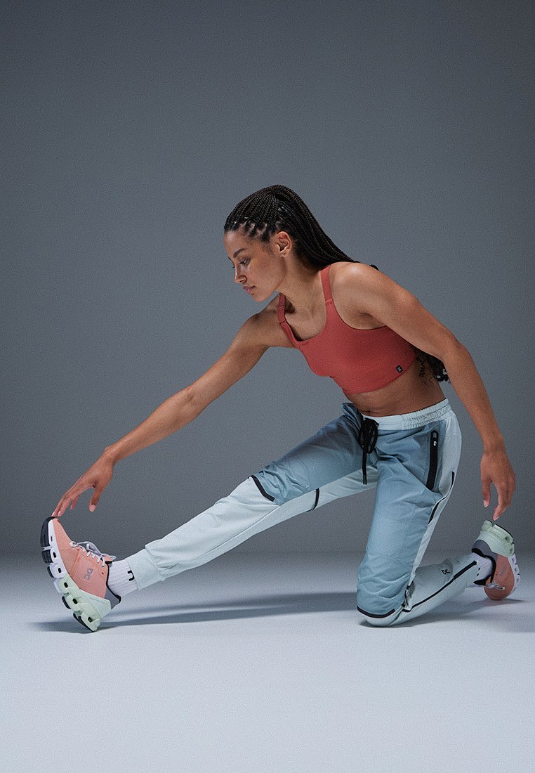 Sportliche Schuhe mit einem rosa und weißen Obermaterial, schwarzen Akzenten und grüner Sohle. Hellblaue Sporthose mit Taschen und Kordelzug.