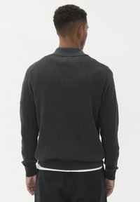 Sötét szürke kötött pulóver ribbelt mintázattal, hosszú ujjak, nyakörv és szoros derékpánt. A hátoldali nézet tiszta vonalakat és egyszerű dizájnt mutat.