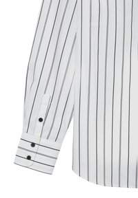 Chemise à manches longues blanche avec des rayures verticales noires. Présente un poignet boutonné avec trois boutons noirs, et un tissu lisse et texturé.