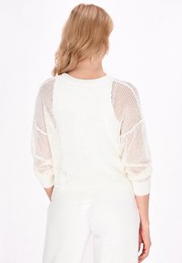 Leichter, cremefarbener Strickpullover mit lockerer Passform, offenem Maschenmuster und gerippten Bündchen und Saum. Die Rückansicht zeigt heruntergesetzte Schulternähte.