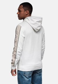 Sudadera blanca con un panel texturizado beige en las mangas, con ribete de contraste y capucha con cordón. Llevada con jeans azules.