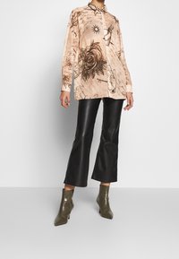 Camicia a maniche lunghe color crema con stampe floreali nere e scritte. Abbinata a pantaloni flared neri lucidi e stivaletti alla caviglia verde oliva.