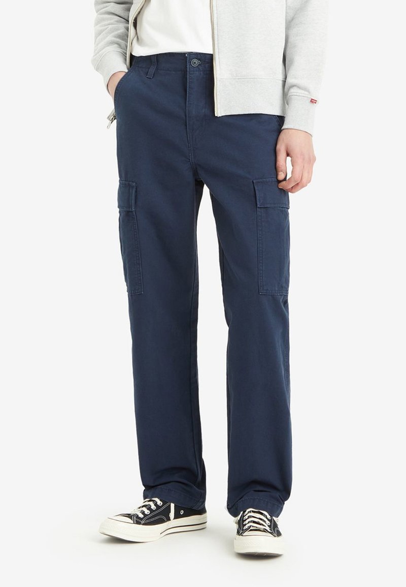 Navy blue cargo pants made of cotton, featuring two side pockets, a straight fit, and a button closure. Paired with black sneakers.