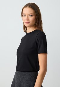 Zwart geribbeld t-shirt met korte mouwen en ronde hals, met een getailleerde pasvorm en een fijne textuur, gecombineerd met een grijze rok.