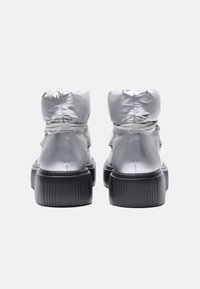 Botines metálico plateado con cuello acolchado, con suelas texturizadas en negro y cierre de cordones para un ajuste ajustable.