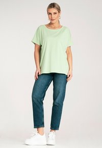 Jasnozielony krótki top z miękkiego materiału, zestawiony z wysokimi niebieskimi dżinsami i białymi trampkami. Prosty i luźny krój.