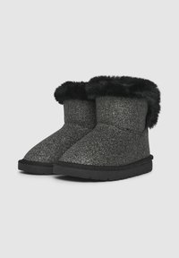 Bottes d'hiver courtes noires pailletées avec bordure en fausse fourrure noire et semelles épaisses noires, sur un fond gris clair uni.