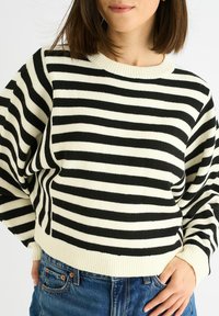 Black and white striped sweater with a ribbed neckline and cuffs, featuring a relaxed fit and soft knit texture. Paired with blue denim jeans.