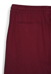Burgunderfarbene Jogginghose mit elastischem Bund, ausgestattet mit einer einzelnen Gesäßtasche mit schmaler Öffnung und einem glatten, strukturierten Stoff.