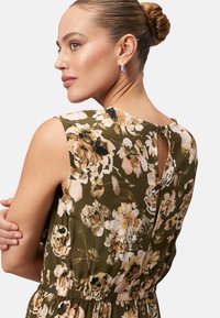 Robe florale avec une base verte ornée de fleurs roses et noires. Design sans manches avec une ouverture en forme de trou de serrure à l'arrière et une taille élastique.
