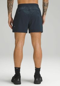 Shorts de sport bleu marine avec une taille élastique, présentant une texture lisse et deux poches latérales, accompagnés de chaussures de course noires.