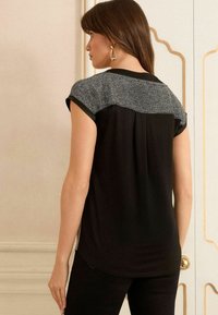 Top scurt negru cu un panou texturat pe umăr de culoare gri. Material moale, tiv rotund și accente negre de-a lungul gulerului.