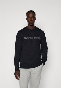 Μαύρο φούτερ με το λογότυπο "BJÖRN BORG" σε λευκό, στρογγυλή λαιμόκοψη, μακριά μανίκια, κατασκευασμένο από μαλακό ύφασμα. Συνδυασμένο με γκρι φόρμες.