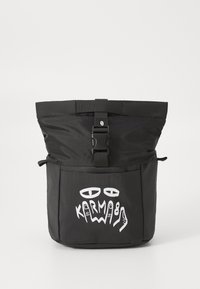 Sac à dos noir avec un dessus repliable, équipé d'une fermeture à clip. La poche frontale présente du texte graphique blanc et des motifs abstraits. Texture de tissu durable.