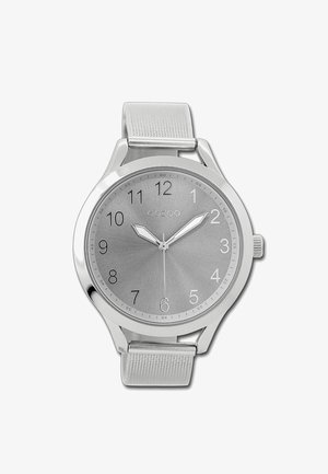 Montre argentée avec un bracelet métallique, cadran rond, fond gris, chiffres arabes et deux aiguilles argentées. Logo de la marque visible en haut.