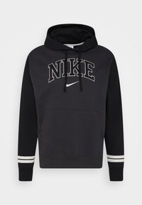 Černá mikina s kapucí a velkým grafickým nápisem "NIKE", klokánkovou kapsou a pruhovanými detaily na manžetách. Disponuje stahovacími šňůrkami a měkkou texturou.