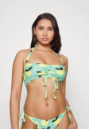 Conjunto de biquíni com um tecido verde pastel com padrões de frutas circulares amarelas. O top tem franzidos elaços; a parte de baixo tem laços laterais. Textura suave.