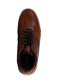 Zapatilla de cuero marrón con una textura suave, cordones oscuros, suela de goma blanca y un sutil detalle lateral en contraste. Punta redondeada, diseño casual.
