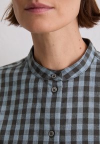 Button-up shirt in blue and black plaid. Features a stand collar and gray buttons. Material appears soft with a slight texture.