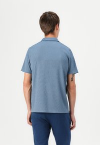 Majica s kratkimi rokavi v modri barvi s strukturiranim vzorcem, ovratnikom in ravnim robom, v kombinaciji s temno modrimi hlačami.