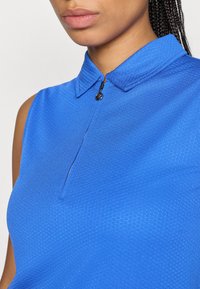 Zila bezpiedurkņu blūze ar apkakles dekoltē un pusi rāvējslēdzēja. Tekstūrēts audums ar nedaudz ģeometrisku rakstu.