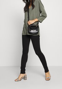 Zwarte skinny jeans gecombineerd met een olijfgroen overhemd met knopen. Een kleine zwarte handtas met krokodillenprint en zebra-print hoge hakken maken de look compleet.