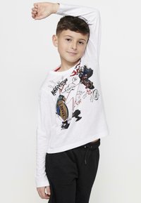 Witte lange mouwen shirt met grafische prints, voorzien van kleurrijke ontwerpen en tekst. Gecombineerd met zwarte sweatpants met trekkoord.