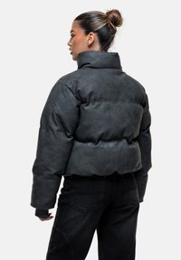 Giacca a vento nera con colletto alto, caratterizzata da una finitura morbida e testurizzata e un design trapuntato e imbottito. Abbinata a pantaloni neri a vita alta.