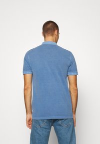 Polo en coton bleu à manches courtes, doté d'un col et d'accents côtelés sur les manches, associé à un jean en denim bleu clair.