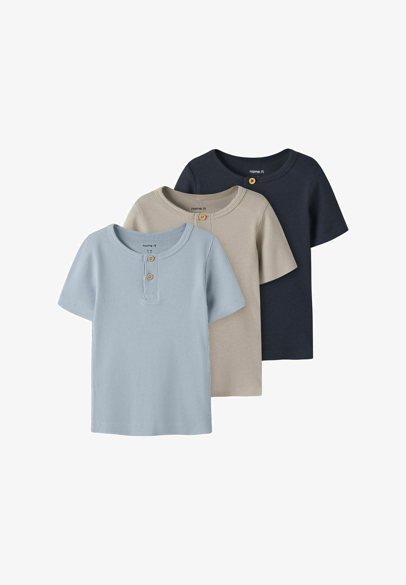 Trīs ribotas īsroku bērnu krekli zilā, bēšā un tumši zilā krāsā, katram ar divām koka pogām pie apaļa kakla izgriezuma.