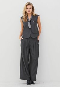 Vest gri cu un decolteu adânc și două buzunare frontale, asociat cu pantaloni gri cu picioare largi, cu pliseuri și o textură fină.