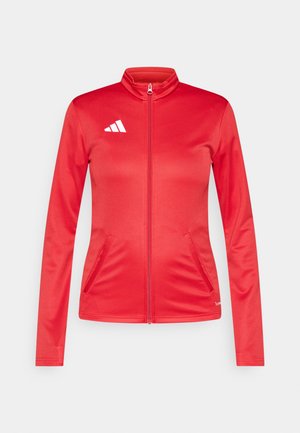 Κόκκινο αθλητικό μπουφάν με φερμουάρ στο εμπρόσθιο μέρος, μακριά μανίκια, δύο πλαϊνές τσέπες και λευκό λογότυπο στο αριστερό στήθος. Λειανός συνθετικός ύφασμα.