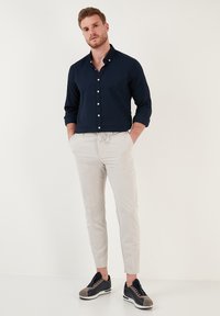 Camisa de botones texturizada en color azul marino, pantalones beige con cordones, y zapatillas grises con detalles en negro, mostrados en un modelo contra un fondo neutro.