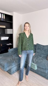 Πράσινη πλεκτή ζακέτα με πέντε κουμπιά, συνδυασμένη με ανοιχτό μπλε τζιν και μια τσάντα σε mint green με ραφή. Μαλακό υφασμάτινο καναπέ στο υπόβαθρο.