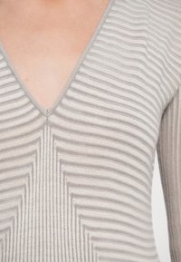 Svetle šedý pletený top s výstřihem do V a vertikálními pruhy, s texturovaným vzorem a přiléhavým střihem, který zdůrazňuje elegantní vzhled.