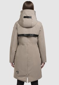 Beige gewatteerde parka met een hoge kraag, een zwarte logoband over de achterkant en een afgeronde zoom. Soepele textuur en minimale hardwaredetails.