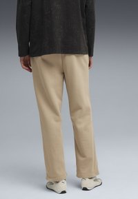 Beige bomulds sweatpants med en afslappet pasform, der har en glat tekstur og manchetter, parret med hvide og sorte træningssko.