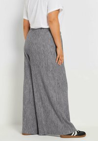 Grå randiga vida byxor med elastisk midja, tillverkade av mjukt tyg, ihop med svarta och vita sneakers.