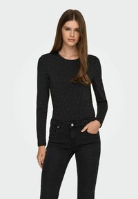 Body nero a maniche lunghe con un sottile motivo a punti argentati, scollo rotondo e design aderente, abbinato a jeans neri. Tessuto dalla texture liscia.