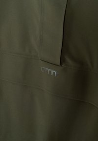 Tissu vert olive avec des détails subtils au niveau des coutures et un petit logo réfléchissant « aimn » imprimé sur la surface.