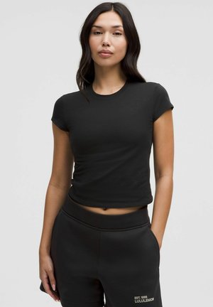 Camiseta ajustada negra con mangas cortas y cuello redondo, hecha de material liso. Se lleva con pantalones cortos de sudadera negros con detalle de logo.