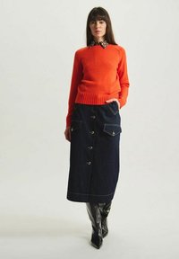 Pull en tricot orange vif avec un col à motifs, associé à une jupe en denim foncé à boutons dotée de poches et de surpiqûres contrastantes.