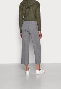 Culottes côtelées grises à coupe ample, associées à un haut à capuche vert olive. Des baskets blanches complètent ce look décontracté.