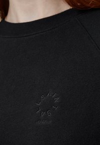 Sudadera negra con cuello redondo, hecha de algodón suave. Presenta un logotipo en relieve con costura tono sobre tono en el lado izquierdo.