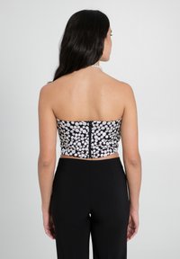 Schwarz-weißer gepunkteter Crop-Top mit taillierter Passform, schulterfreiem Schnitt und Reißverschluss im Rücken, kombiniert mit schwarzen Hosen.